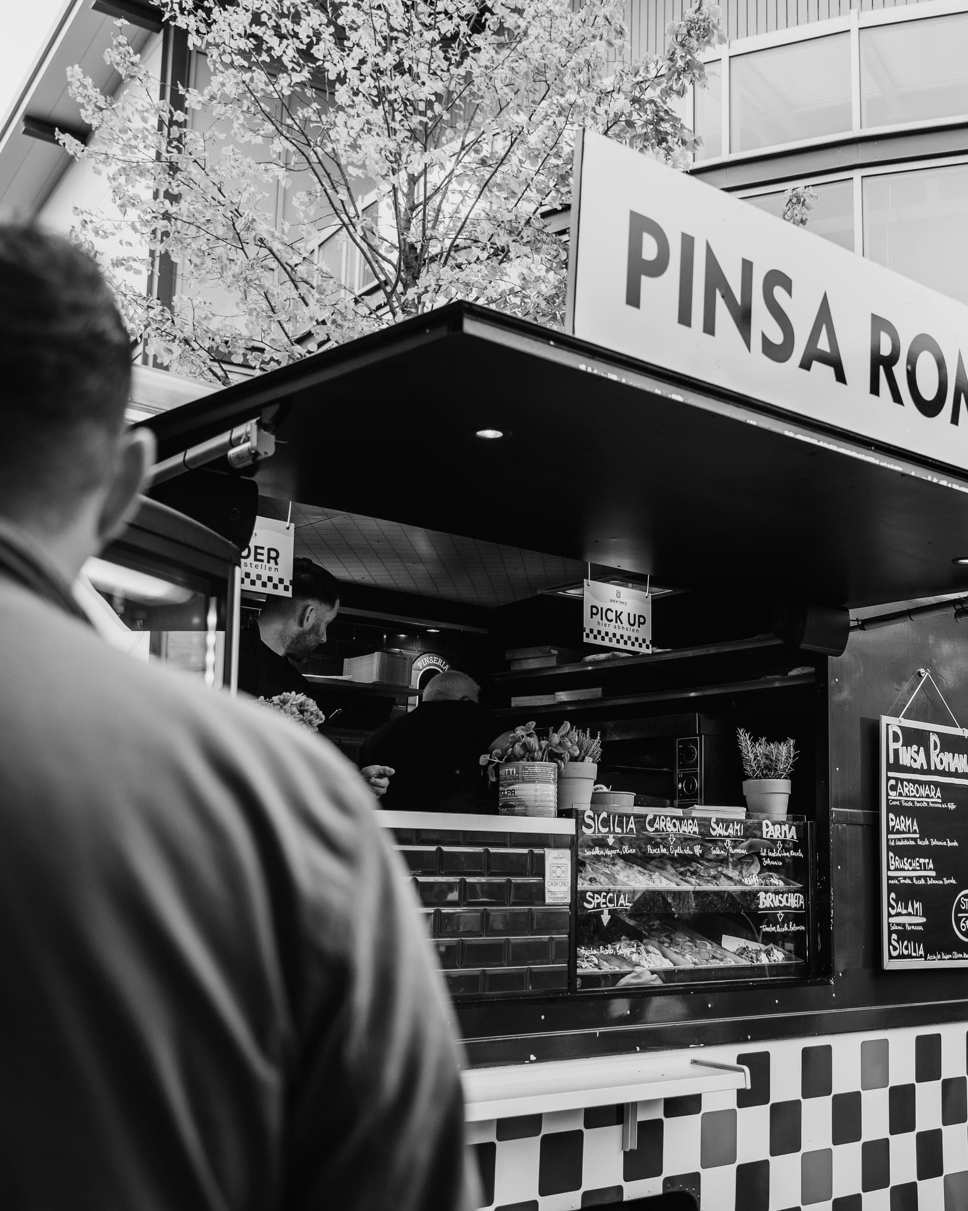 Ein Gast wartet an der offenen Theke, während das Team im Pinsa-Foodtruck arbeitet