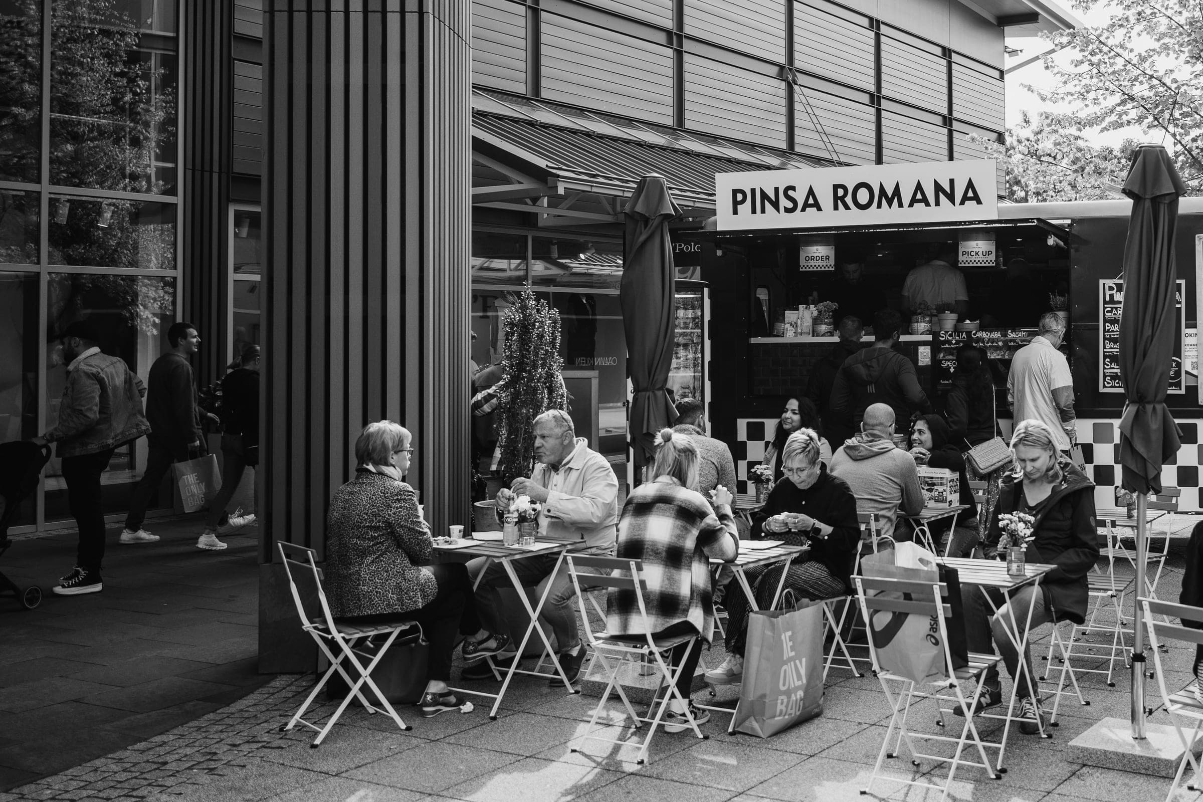 Gäste sitzen mit ihrem Essen vor der offenen Theke unseres Pinsa-Foodtrucks im Außenbereich